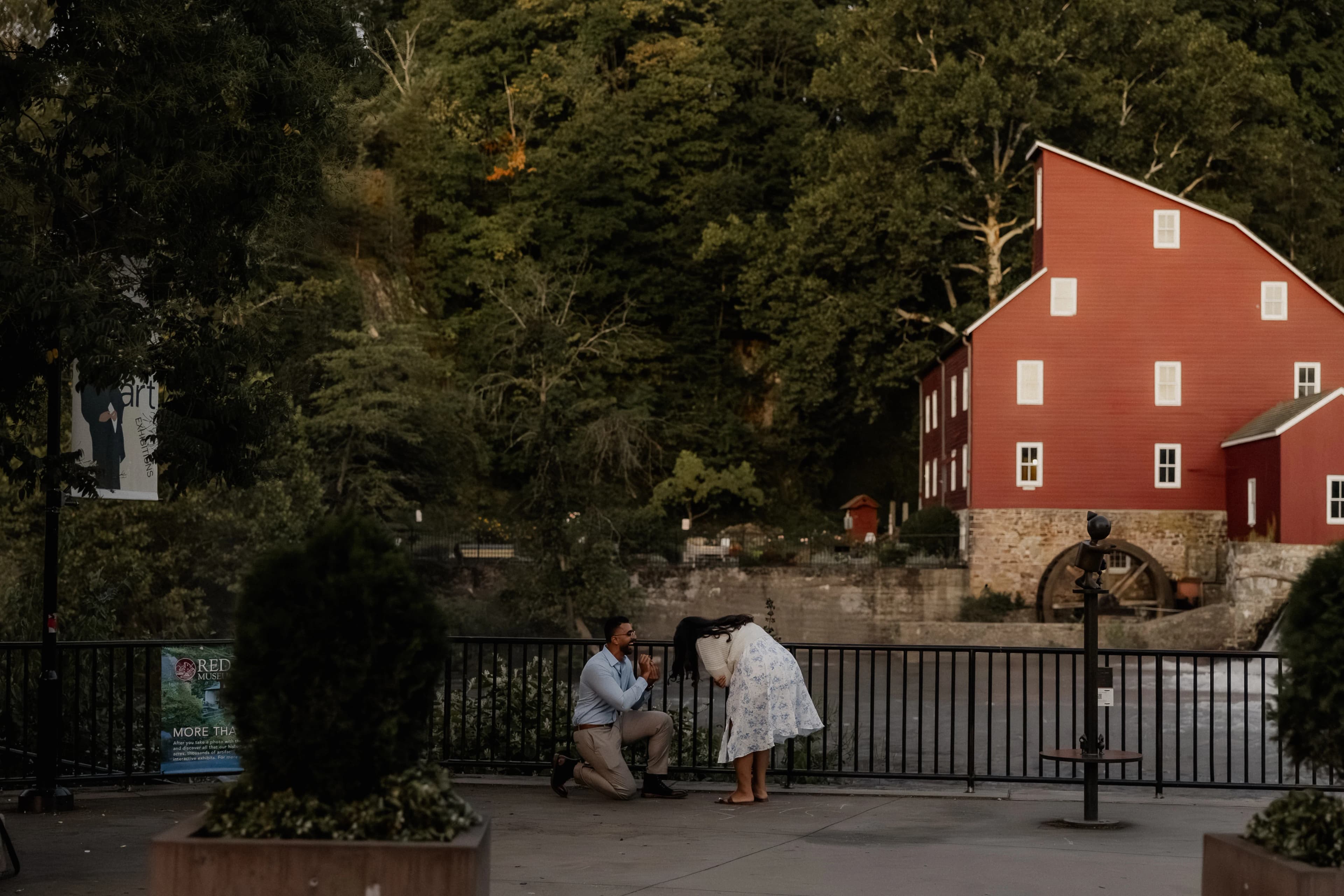Anthony on one knee proposing to Lily beside the river at the Red Mill
