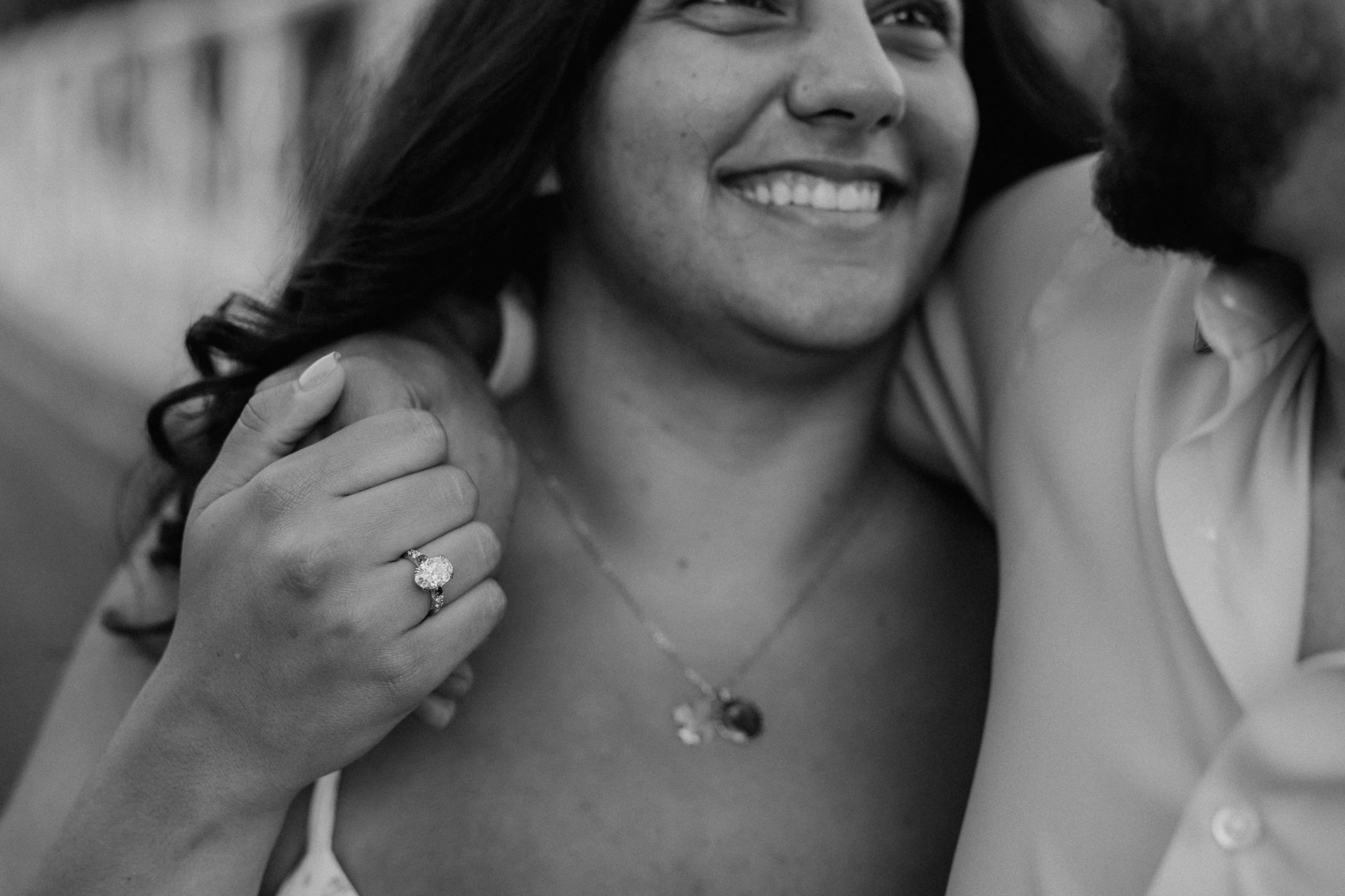 Black and white close-up of Lily smiling, her engagement ring on her hand